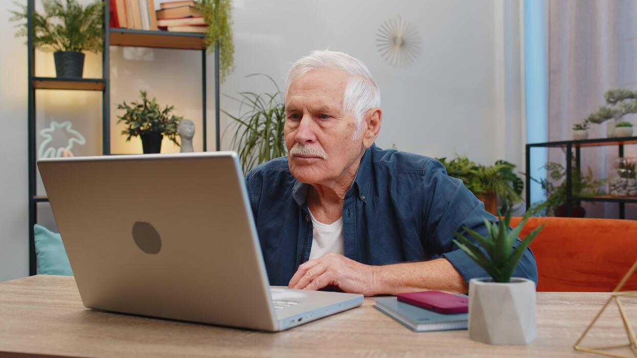A senior woman smiling while using a laptop at home